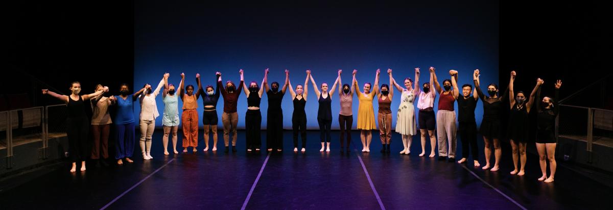 Many dancers in a semi-circle, hands linked and raised for a bow.